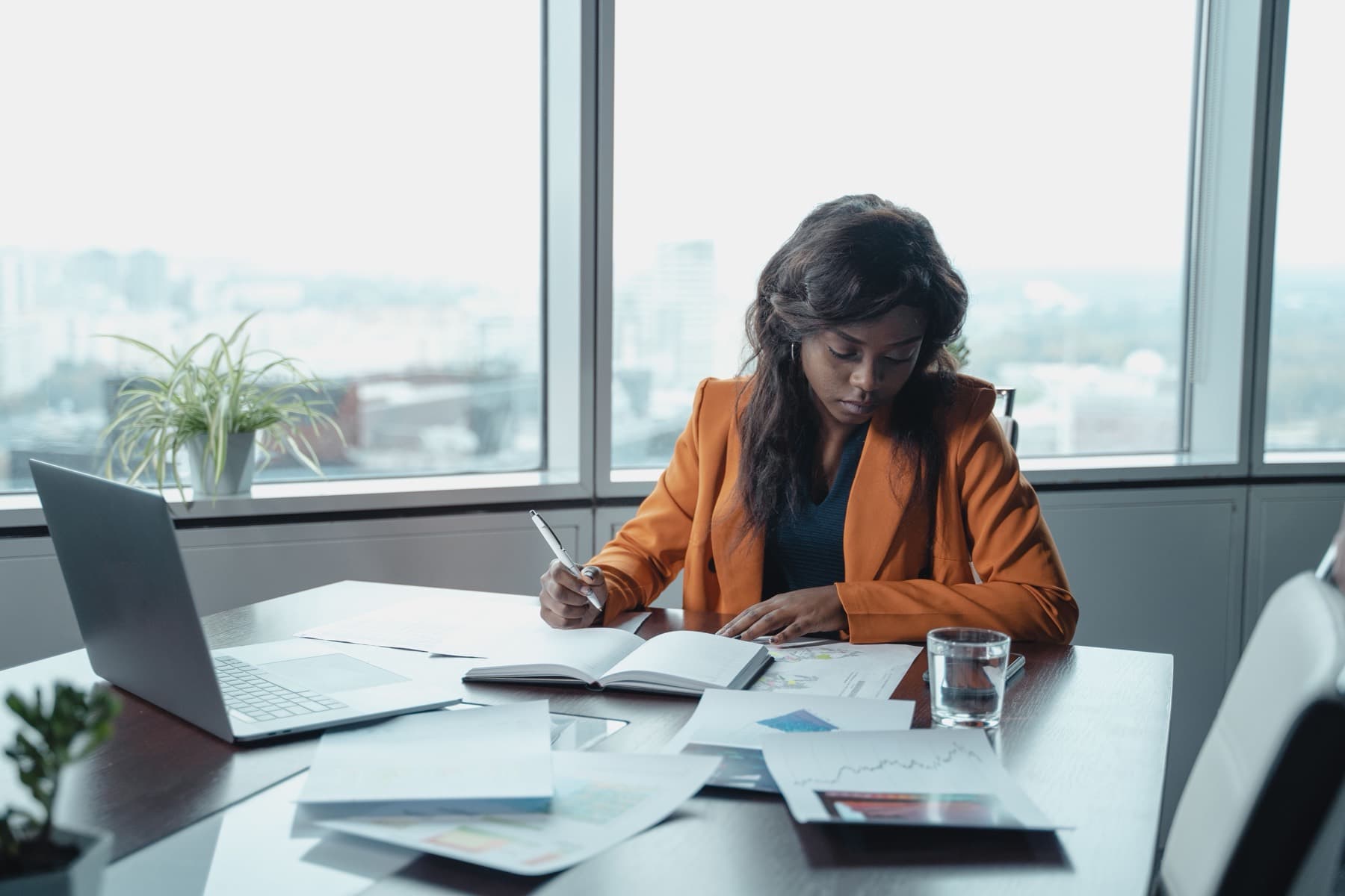 A woman in an orange blazer working through documents at an office desk